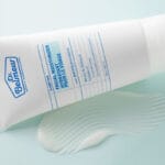Dr. Belmeur Clarifying Facial Moisturizer 120ml – leichte Feuchtigkeitscreme für zu Akne neigende Haut mit Niacinamid und Panthenol. Abbildung Produkt mit Creme im Hintergrund, Nahaufnahme.