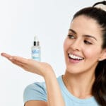 Dr. Belmeur Spot Care Ampoule 22ml - soothing serum with panthenol, beta-glucan, chaga mushroom and tea tree oil against blemishes and redness. Image of smiling woman holding the product. 